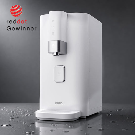 Produktfoto des weißen NAIS Ambient Wasserspenders in minimalistischem Design auf einer dunklen, reflektierenden Oberfläche mit Wassertropfen. Links im Bild ist das rote Siegel ‚reddot Gewinner‘ zu sehen.